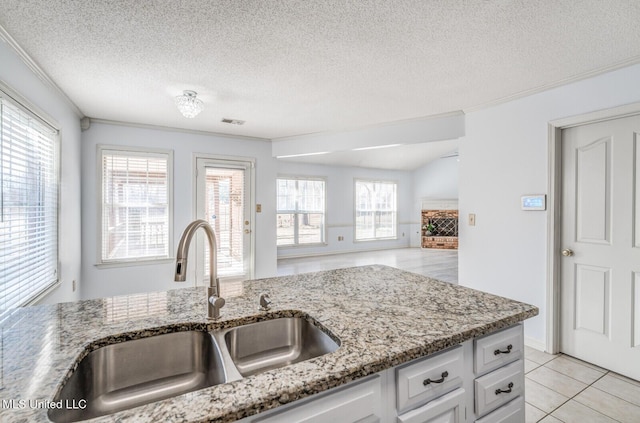 kitchen with a textured ceiling, sink, white cabinetry, plenty of natural light, and light tile patterned flooring