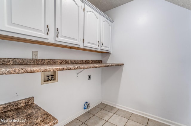 laundry room with hookup for an electric dryer, light tile patterned floors, a textured ceiling, and cabinets