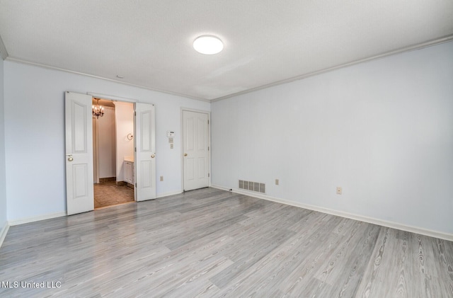 unfurnished bedroom featuring ensuite bath, crown molding, light hardwood / wood-style flooring, and an inviting chandelier