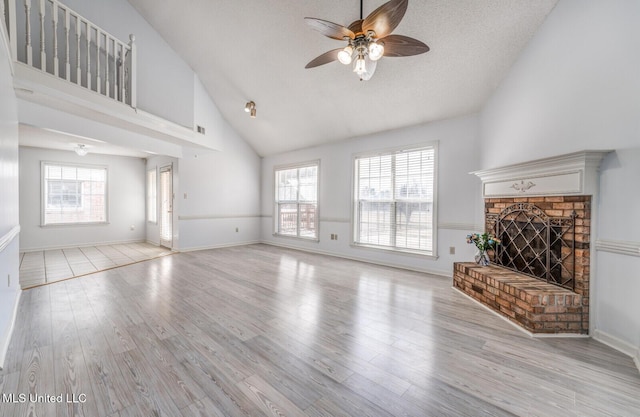 unfurnished living room with ceiling fan, light wood-type flooring, a textured ceiling, and a brick fireplace