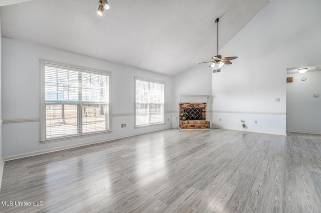 unfurnished living room featuring a brick fireplace, ceiling fan, lofted ceiling, and light hardwood / wood-style flooring