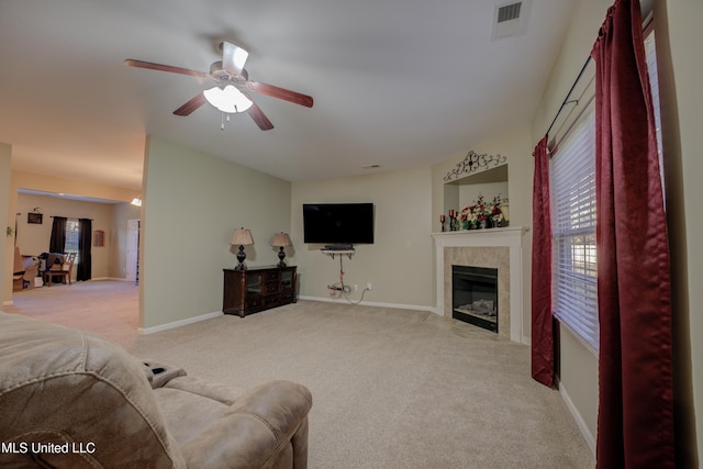 living room featuring a tiled fireplace, ceiling fan, and light colored carpet