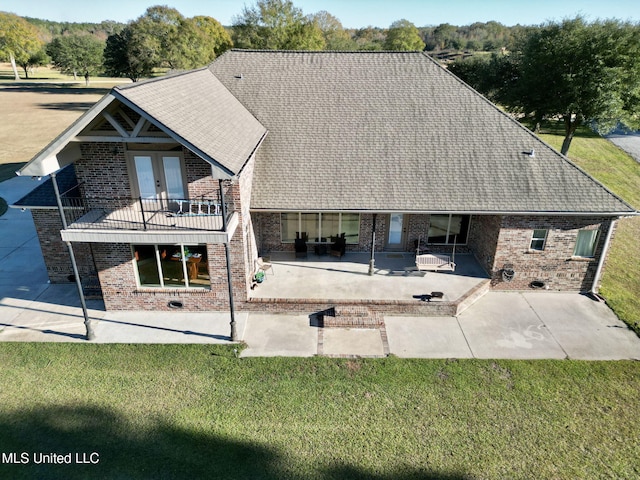 rear view of property featuring a lawn, a balcony, and a patio