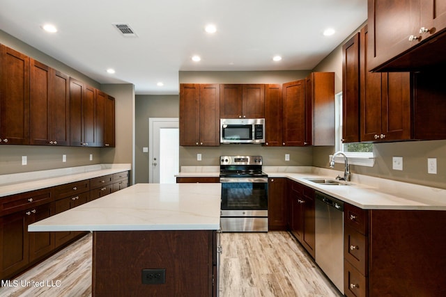 kitchen featuring light stone countertops, appliances with stainless steel finishes, sink, light wood-type flooring, and a kitchen island