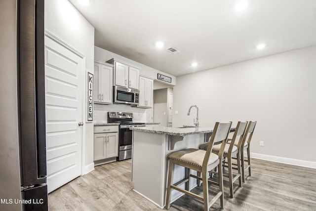 kitchen featuring tasteful backsplash, light wood-type flooring, a kitchen bar, appliances with stainless steel finishes, and a sink