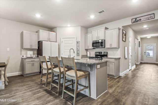 kitchen featuring visible vents, a center island with sink, a kitchen breakfast bar, dark wood finished floors, and appliances with stainless steel finishes