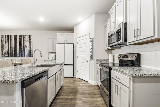 kitchen with light stone countertops, a sink, decorative backsplash, dark wood-type flooring, and appliances with stainless steel finishes