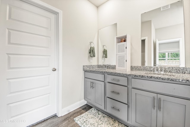 full bath with double vanity, wood finished floors, baseboards, and a sink