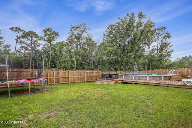 view of yard featuring a fenced backyard, a fenced in pool, a wooden deck, and a trampoline