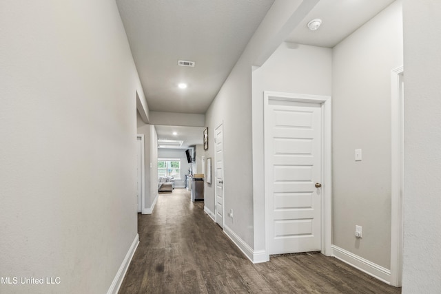 hall with visible vents, baseboards, and dark wood-style flooring