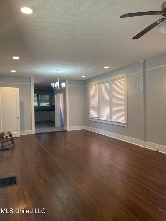 unfurnished living room featuring ceiling fan with notable chandelier and dark hardwood / wood-style floors