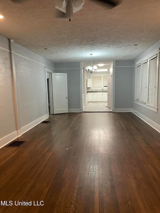 interior space with a textured ceiling, ceiling fan with notable chandelier, and dark hardwood / wood-style floors