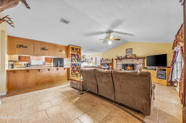 tiled living room with ceiling fan, a fireplace, and vaulted ceiling