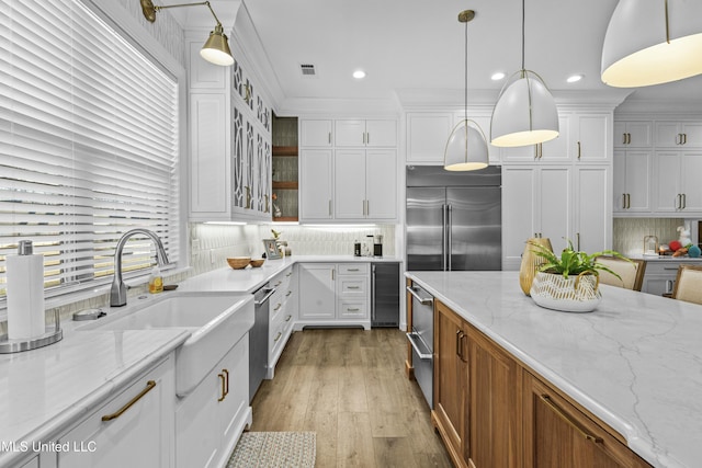 kitchen featuring visible vents, stainless steel built in fridge, a sink, glass insert cabinets, and white cabinetry