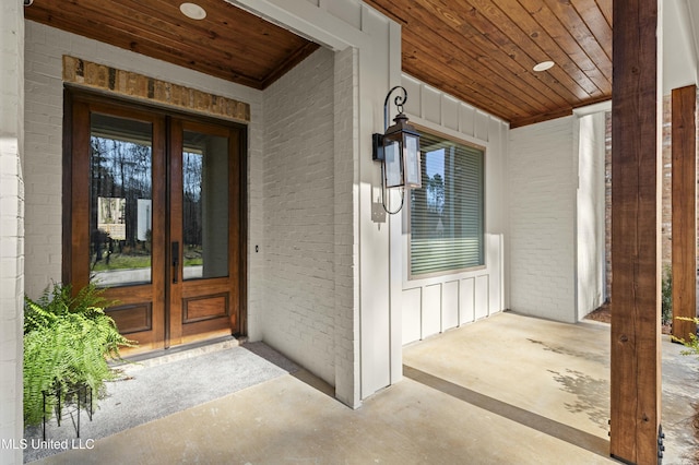 doorway to property featuring brick siding, a porch, french doors, and board and batten siding