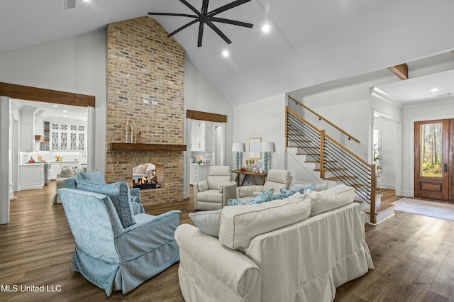 living room featuring stairway, a fireplace, wood finished floors, high vaulted ceiling, and a ceiling fan