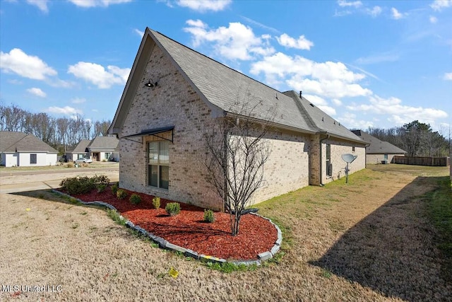 view of side of home featuring a yard, brick siding, and a shingled roof