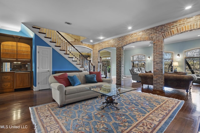 living area featuring dark wood-type flooring, brick wall, crown molding, and ornate columns