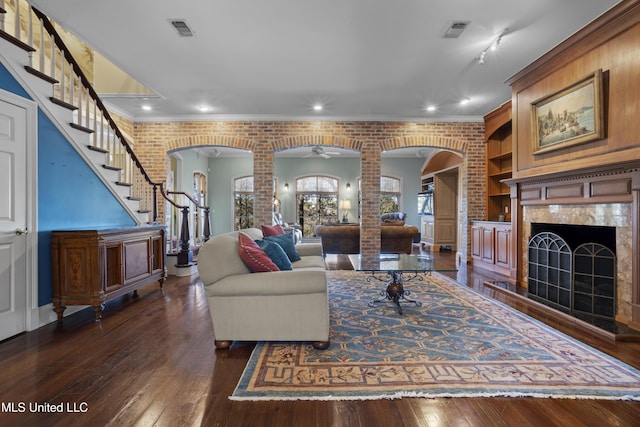 living room with a fireplace, dark wood-type flooring, arched walkways, and visible vents