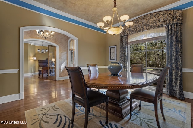 dining space with crown molding, baseboards, wood finished floors, arched walkways, and a notable chandelier