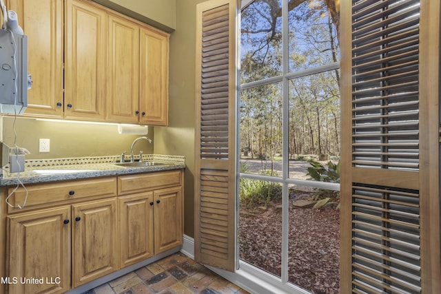 kitchen featuring light stone countertops, brick floor, and a sink