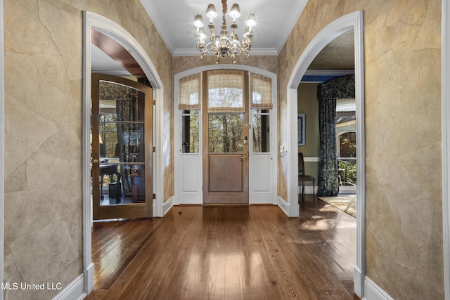 foyer entrance with arched walkways, a notable chandelier, crown molding, and wood-type flooring