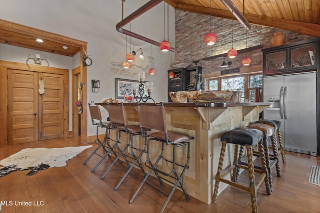 bar featuring high vaulted ceiling, wood finished floors, stainless steel fridge with ice dispenser, and a dry bar