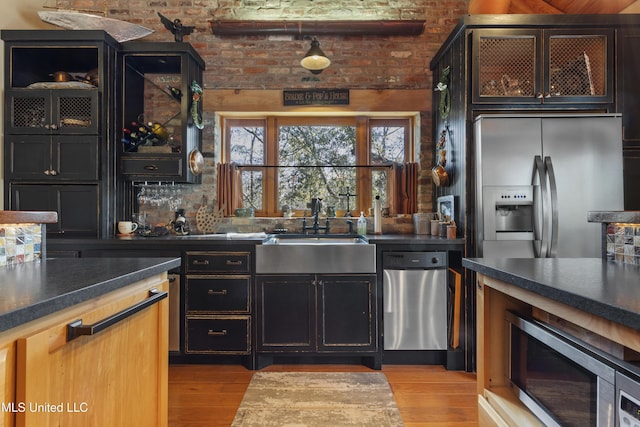 kitchen with a sink, dark countertops, appliances with stainless steel finishes, and light wood finished floors