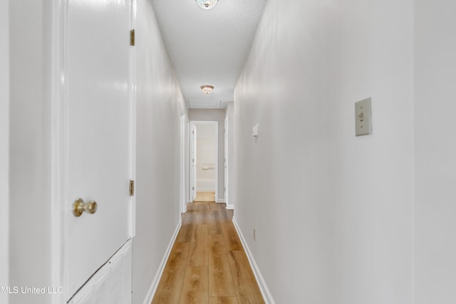 hall featuring baseboards, attic access, and light wood-style flooring