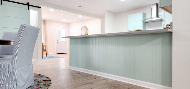 interior space featuring a barn door, light wood-style floors, wall chimney range hood, a peninsula, and baseboards