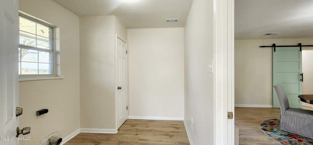 interior space with visible vents, light wood-style flooring, baseboards, and a barn door