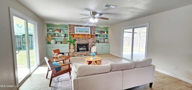 living area featuring light wood finished floors, baseboards, visible vents, built in shelves, and a fireplace