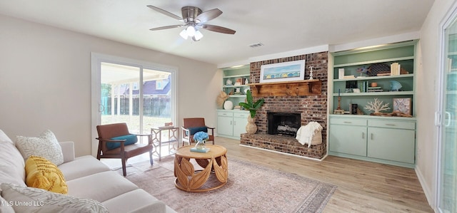 living room featuring built in features, a fireplace, light wood finished floors, visible vents, and a ceiling fan