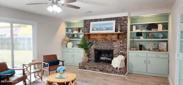 living area with built in features, a fireplace, visible vents, light wood-style flooring, and ceiling fan