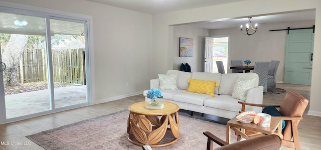 living area featuring light wood-type flooring, a barn door, a chandelier, and baseboards