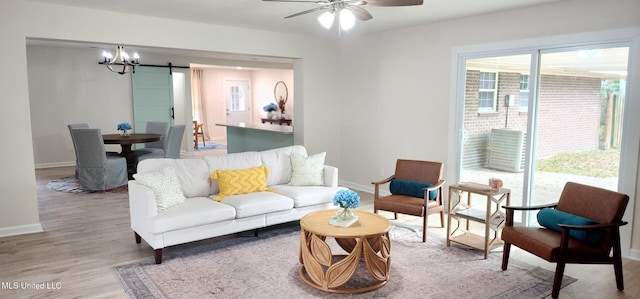 living area featuring a barn door, baseboards, wood finished floors, and ceiling fan with notable chandelier