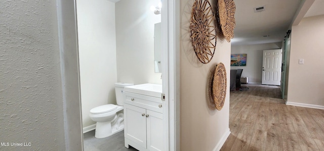 bathroom with toilet, wood finished floors, vanity, visible vents, and baseboards