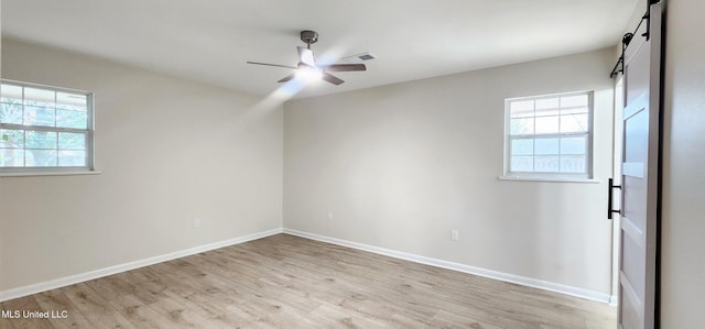 unfurnished bedroom featuring visible vents, light wood-style flooring, a barn door, a ceiling fan, and baseboards