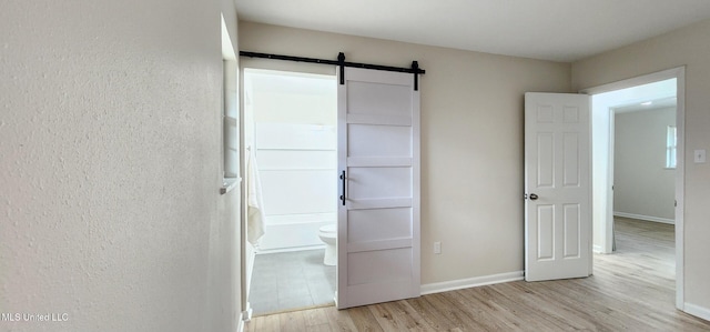 unfurnished bedroom with a barn door, baseboards, and light wood-style flooring