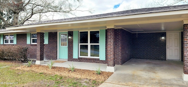 property entrance with a carport, brick siding, and concrete driveway