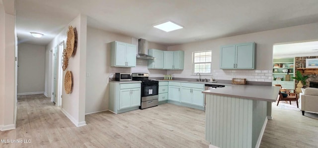 kitchen with a peninsula, a sink, appliances with stainless steel finishes, wall chimney exhaust hood, and light wood finished floors