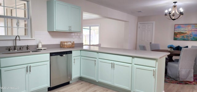 kitchen featuring light countertops, hanging light fixtures, stainless steel dishwasher, a sink, and a peninsula