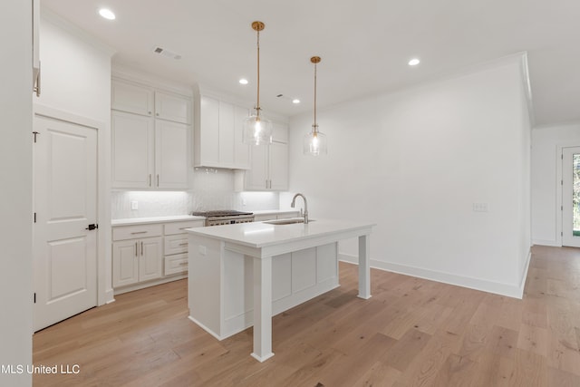 kitchen featuring an island with sink, stainless steel stove, sink, pendant lighting, and light wood-type flooring