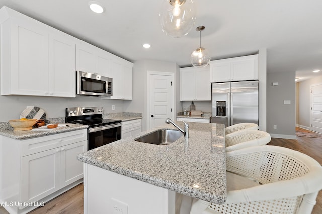 kitchen with appliances with stainless steel finishes, a sink, light wood-style floors, white cabinets, and a kitchen island with sink