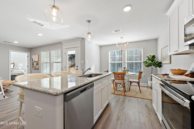 kitchen featuring stainless steel appliances, a sink, light wood-style floors, a kitchen island with sink, and white cabinetry