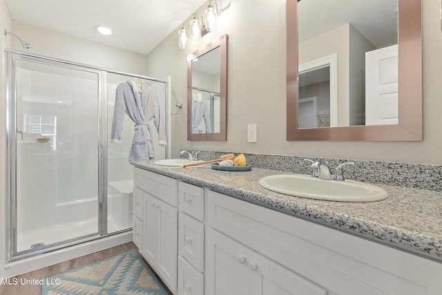full bathroom with a shower stall, wood finished floors, and double vanity