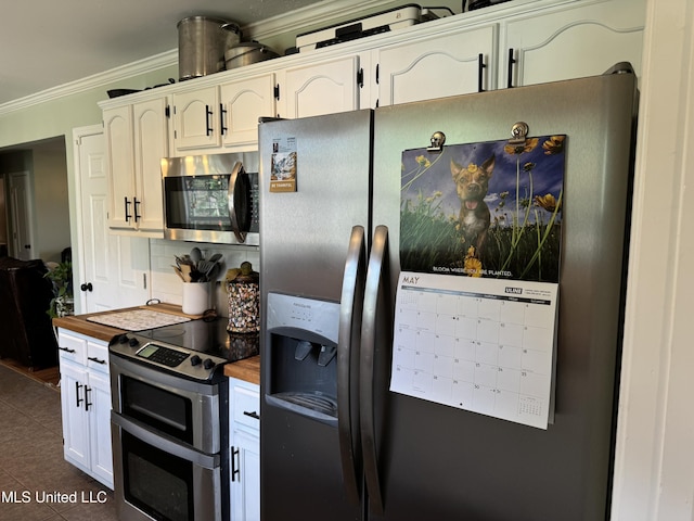 kitchen with white cabinetry, stainless steel appliances, dark tile patterned floors, butcher block countertops, and ornamental molding