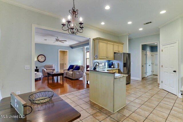 kitchen with stainless steel refrigerator with ice dispenser, ornamental molding, pendant lighting, light tile patterned floors, and ceiling fan with notable chandelier