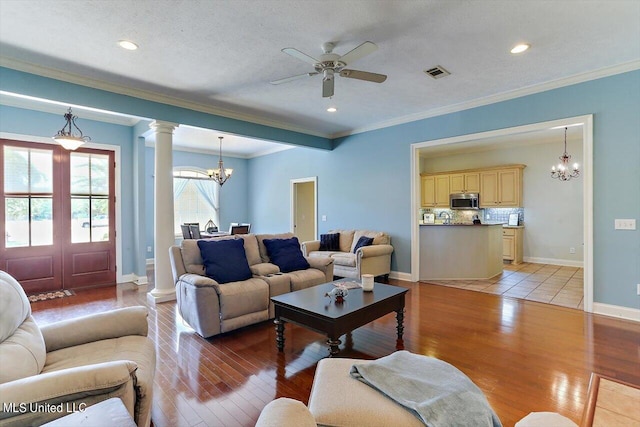 living room with a textured ceiling, light wood-type flooring, decorative columns, ornamental molding, and ceiling fan with notable chandelier