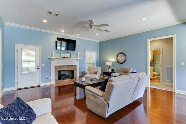 living room featuring ceiling fan, a textured ceiling, ornamental molding, dark hardwood / wood-style floors, and a fireplace